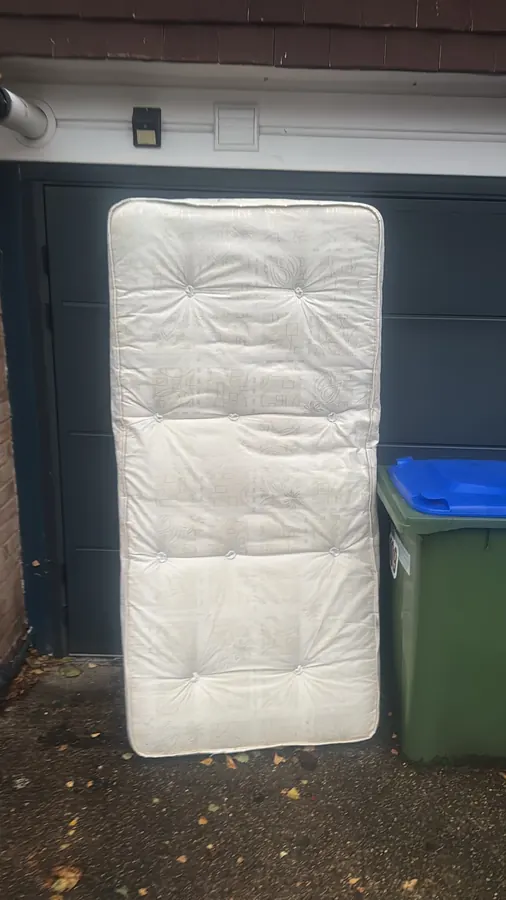 Single mattress waiting for collection outside a garage